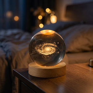 Lampe galaxie en boule de cristal gravée en 3D posée allumée sur une table de chevet