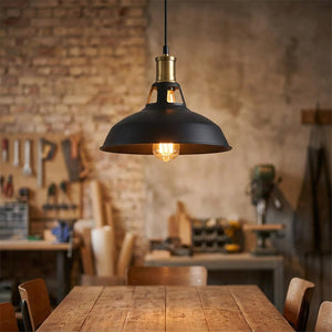 Suspension industrielle vintage à abat-jour en métal noir allumée au-dessus d'une table dans un intérieur de style atelier