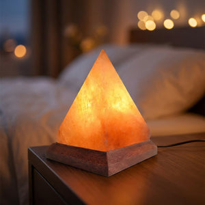 Lampe pyramide en sel de l'Himalaya allumée en orange sur une table de chevet en bois