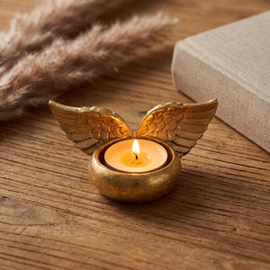 Bougeoir ailes d'ange en résine dorée avec bougie allumée sur table en bois ambiance romantique