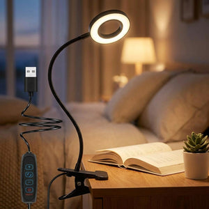 Lampe pince noire à col de cygne allumée avec lumière chaude clipsée sur une table de nuit en bois