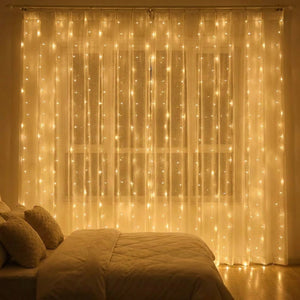 Rideau lumineux LED doré suspendu à une fenêtre dans une chambre chaleureuse avec lit cocooning
