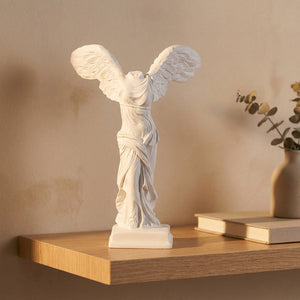 Statue blanche de la déesse grecque de la victoire ailée posée sur une étagère en bois