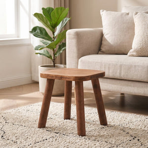 Petit tabouret carré en bois massif noyer posé sur un tapis dans un salon chaleureux