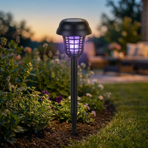 Lampe solaire anti-moustiques noire plantée dans un jardin diffusant une lumière violette au crépuscule