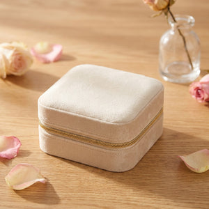 Boîte à bijoux en velours beige avec fermeture éclair dorée posée sur une surface en bois avec pétales de rose