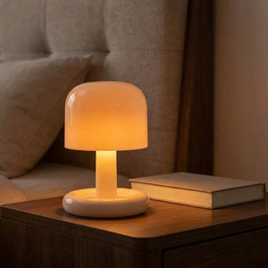 Lampe champignon beige allumée diffusant une lumière chaude posée sur une table de chevet en bois