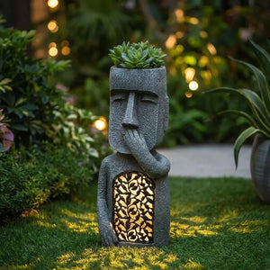 Statue Moai île de Pâques en résine grise dans un jardin au crépuscule avec panneau lumineux et plante