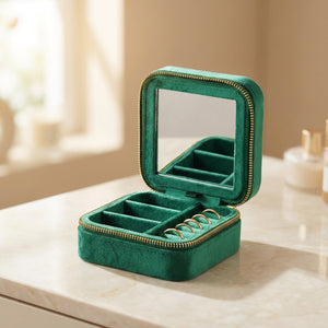Boîte à bijoux de voyage en velours vert émeraude ouverte avec miroir intégré et bagues posée sur une coiffeuse