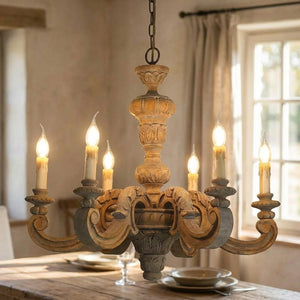 Lustre en bois sculpté à six bras et bougies stylisées suspendu au-dessus d'une table de salle à manger