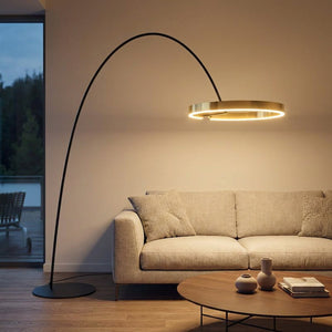Lampadaire arc italien anneau LED doré allumé au-dessus d'un canapé dans un salon chaleureux