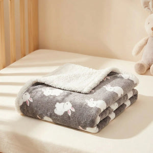 Couverture bébé grise motif lapins blancs doublée peluche sherpa posée sur un lit de berceau