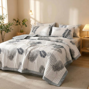 Couette d'été imprimée feuillage gris posée sur un lit fait dans une chambre lumineuse