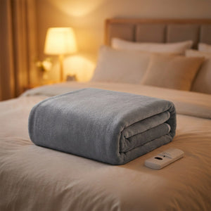 Couverture chauffante électrique grise pliée avec sa télécommande sur un lit