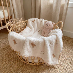 Couverture bébé en flanelle crème brodée de petits oursons posée dans un lit bébé douillet