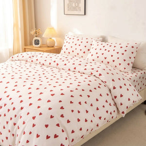 Parure de lit 3 pièces à motif petit cœur rouge sur fond crème installée sur un lit dans une chambre lumineuse