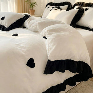 Parure de lit blanche avec housse de couette et taies brodées d un coeur noir sur un lit fait dans une chambre lumineuse
