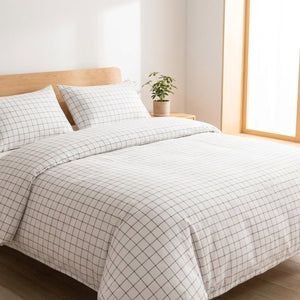 Parure de lit blanche à fines lignes noires installée sur un lit dans une chambre lumineuse