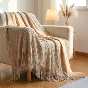 Plaid tricoté beige aux losanges en relief avec franges drapé sur un canapé dans un salon chaleureux