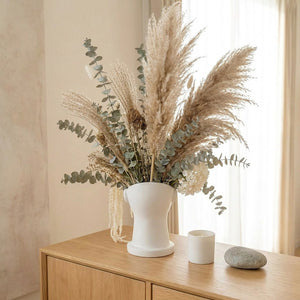 Vase décoratif blanc style antique avec arrangement de pampa et eucalyptus sur commode en chêne, intérieur scandinave