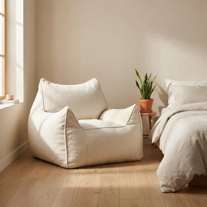 Housse de pouf bouclé beige forme fauteuil près d'un lit dans une chambre lumineuse