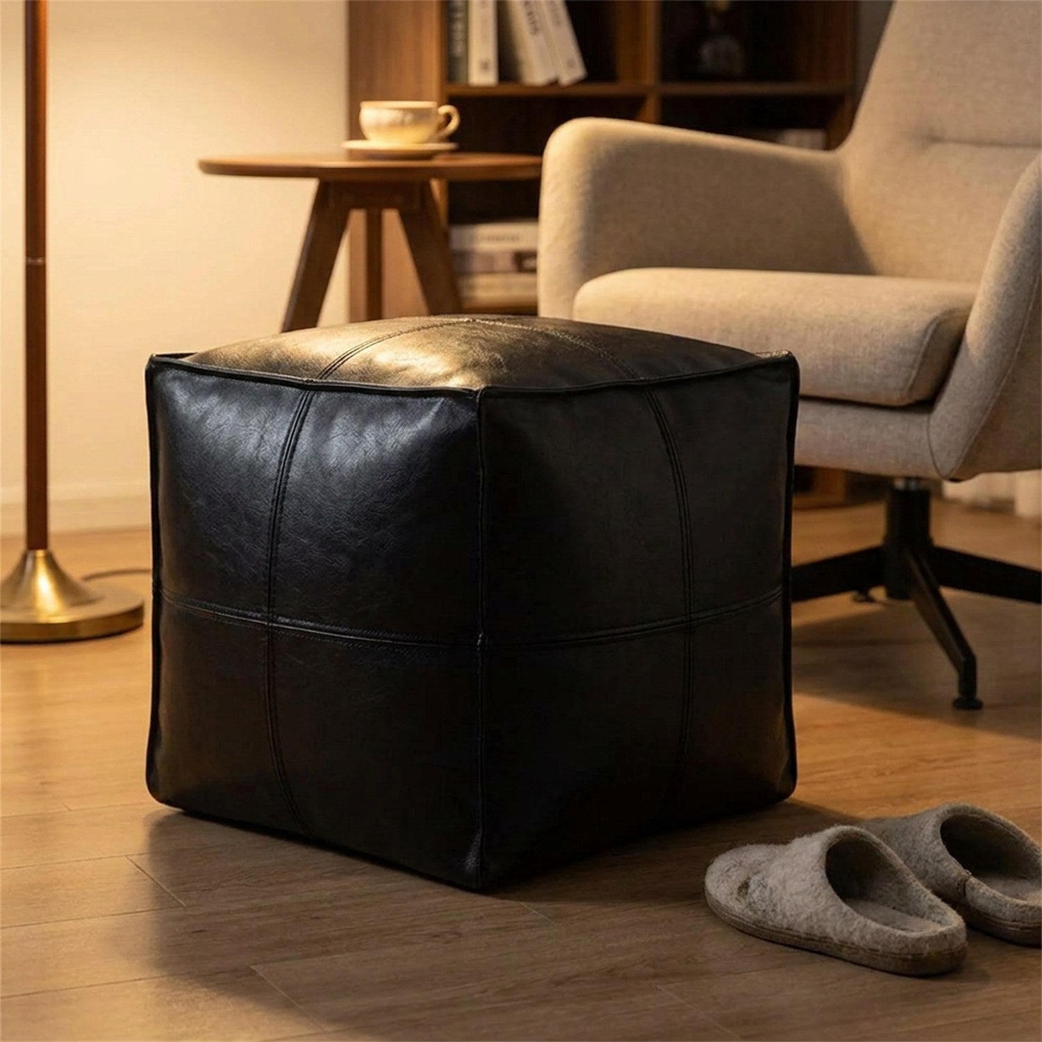 Pouf cube en cuir noir utilisé comme repose-pieds devant un fauteuil de lecture