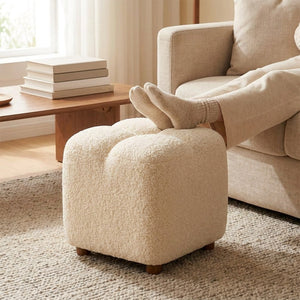 Pouf bouclé blanc utilisé comme repose pieds devant un canapé beige en salon