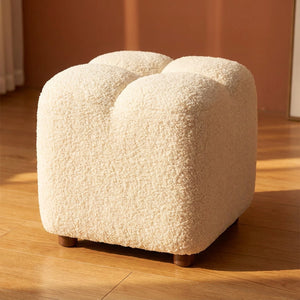 Petit pouf cube en tissu bouclé effet laine d'agneau blanc posé sur un parquet chaleureux