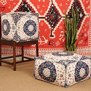 Housse de pouf marocain ivoire à motif floral bleu marine posée sur tapis berbère