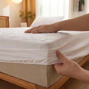 Mains ajustant la jupe élastique du protège-matelas blanc sur un matelas