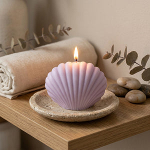 Bougie coquillage violet allumée sur une coupelle en pierre dans une ambiance zen