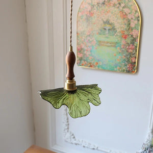 Suspension feuille en verre vert et bois de noyer devant un cadre fleuri