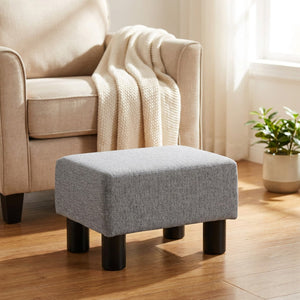 Repose-pieds tabouret bas rembourré en tissu gris posé près d un fauteuil