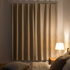 Rideau occultant beige fermé dans une chambre la nuit avec lampe de chevet