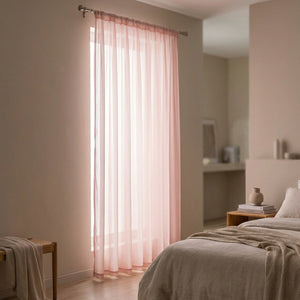 Voilage uni rose suspendu à une fenêtre dans une chambre douce