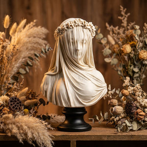 Sculpture de buste voilé en résine gris clair posé sur une étagère en bois avec des fleurs séchées fond ambré