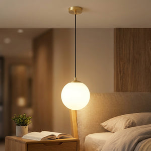 Suspension boule de verre opale dorée en lumière chaude près d'une table de chevet