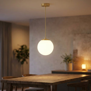 Suspension globe en verre opale blanc à finition dorée allumée au-dessus d'une table à manger