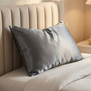 Taie d'oreiller en satin effet soie gris foncé posée sur un lit