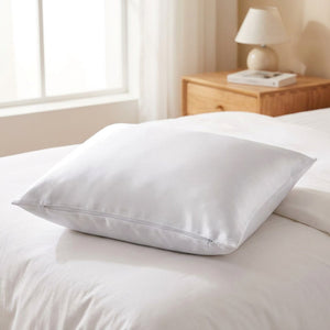 Taie d'oreiller en satin blanc soyeux avec fermeture éclair posée sur un lit clair lumineux