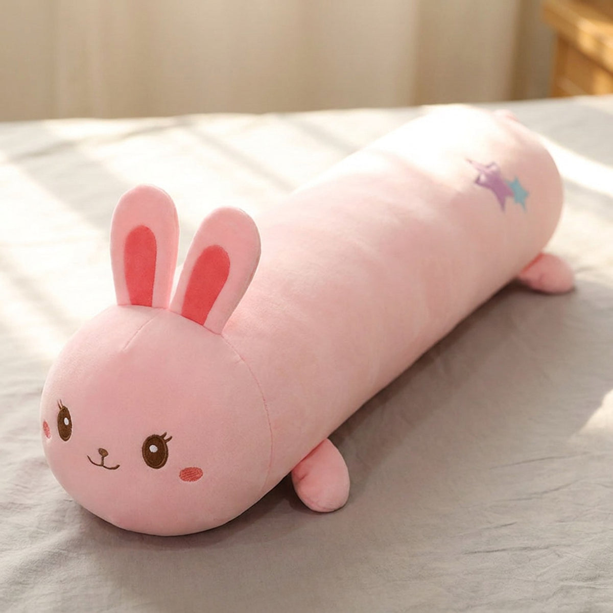 Traversin peluche en forme de lapin kawaii posé sur un lit clair