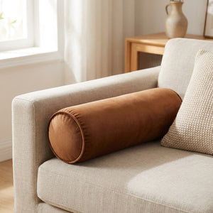 Traversin cylindrique en velours marron posé sur un canapé beige