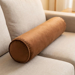 Traversin cylindrique en velours marron sur un canapé beige