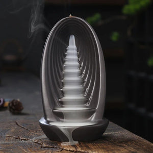 Brûleur d'encens à reflux en céramique vu de trois quarts avec fumée cascadant sur une table en bois