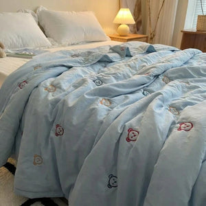 Couette d'été bleue brodée de petits oursons posée sur un lit