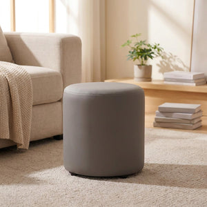 Tabouret pouf rond gris posé sur un tapis près d'un canapé beige