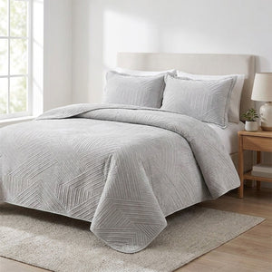 Couvre-lit matelassé en velours gris clair au motif géométrique brodé sur un lit