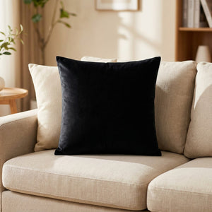 Housse de coussin en velours noir posée sur un canapé en lin clair