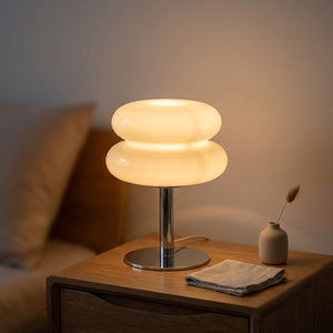 Lampe de chevet en verre forme macaron beige allumée sur une table de nuit