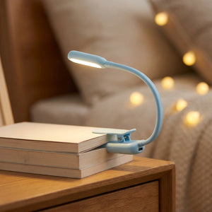 Lampe de lecture à clipser bleue allumée posée sur une pile de livres